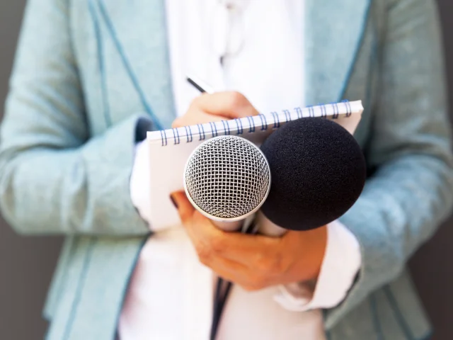 Weibliche Reporterin bei Pressekonferenz, schreibt Notizen, hält Mikrofon